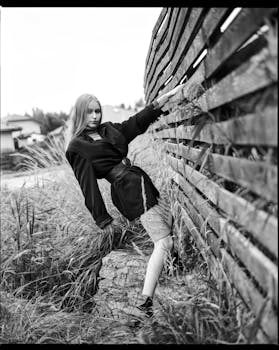 Black and white photo of a stylish woman posing against a fence in Moscow's outdoors.