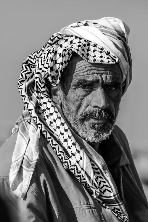 A Grayscale Photo of and Elderly Man Wearing a Scarf on His Head