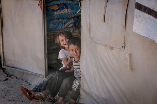 Free Two children smiling while sitting in a Syrian refugee camp doorway, conveying happiness and resilience. Stock Photo
