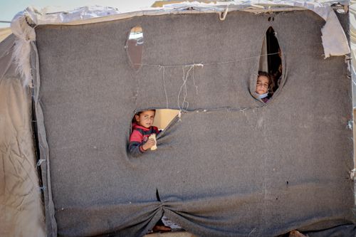 Free Children peeking through a makeshift tent in Idlib, highlighting resilience and hope. Stock Photo