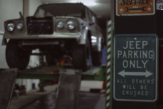 A classic Jeep on a garage lift with a humorous parking sign visible.