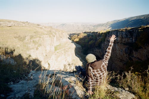Free Person in Brown and White Plaid Shirt Sitting on Rocky Cliff Stock Photo