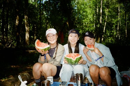 Free Three friends happily eating watermelon together in a summer forest setting. Stock Photo