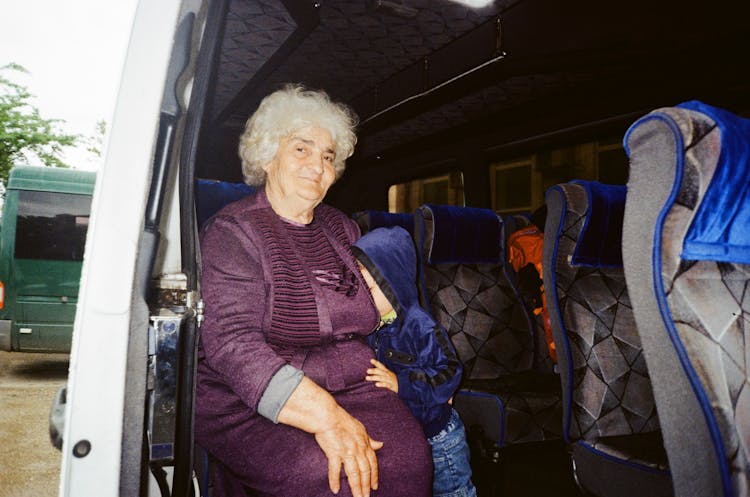 An Elderly Woman Sitting Inside The Car With His Grandchild Beside Her