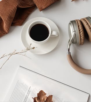 Flat lay of a cozy desk featuring coffee, headphones, and autumn accessories for a relaxing day.