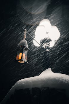 Illuminated street lamp with a hanging lantern during a snowy winter night.
