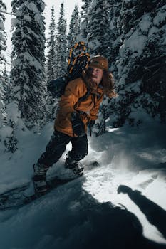 A snowboarder in warm clothing rides through a snow-covered pine forest in winter.