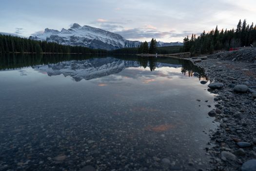 Tranquil lake with snow-capped mountains reflecting in the water during sunset in Banff National Park, Canada.