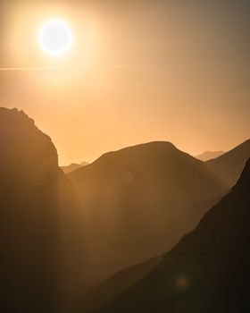 Sunset over silhouetted mountains with warm colors and golden sunbeams creating a dramatic skyline.