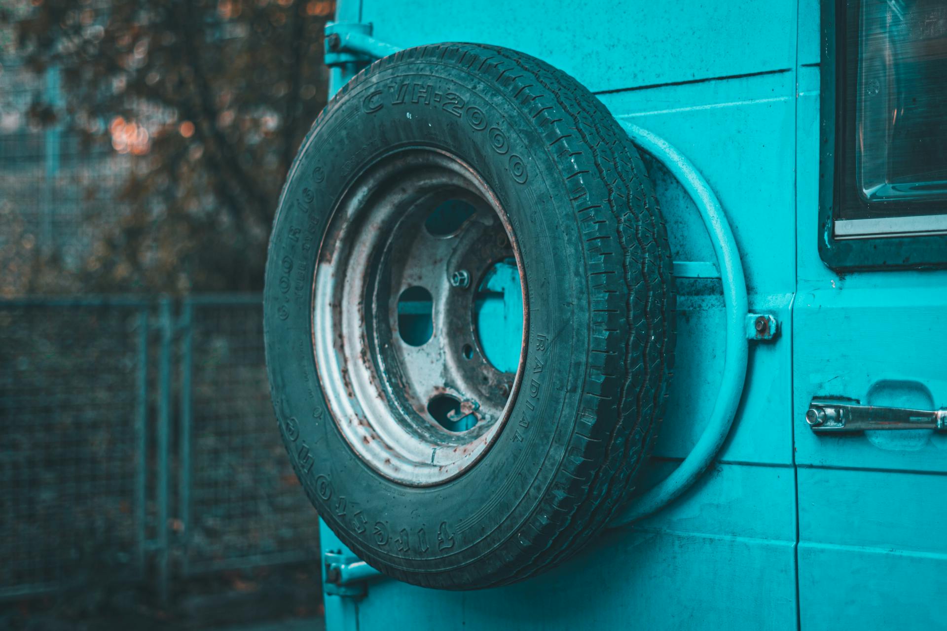 Close-up of a mounted spare tire on a teal vehicle in daylight. Outdoors scene.