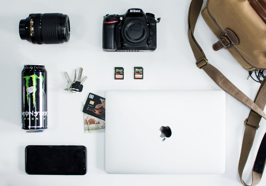 Flat lay of camera, laptop, and tech essentials on a white surface, showcasing everyday items.