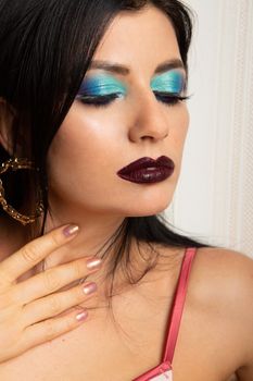 Close-up of woman with dramatic eye makeup and lipstick posing in studio.