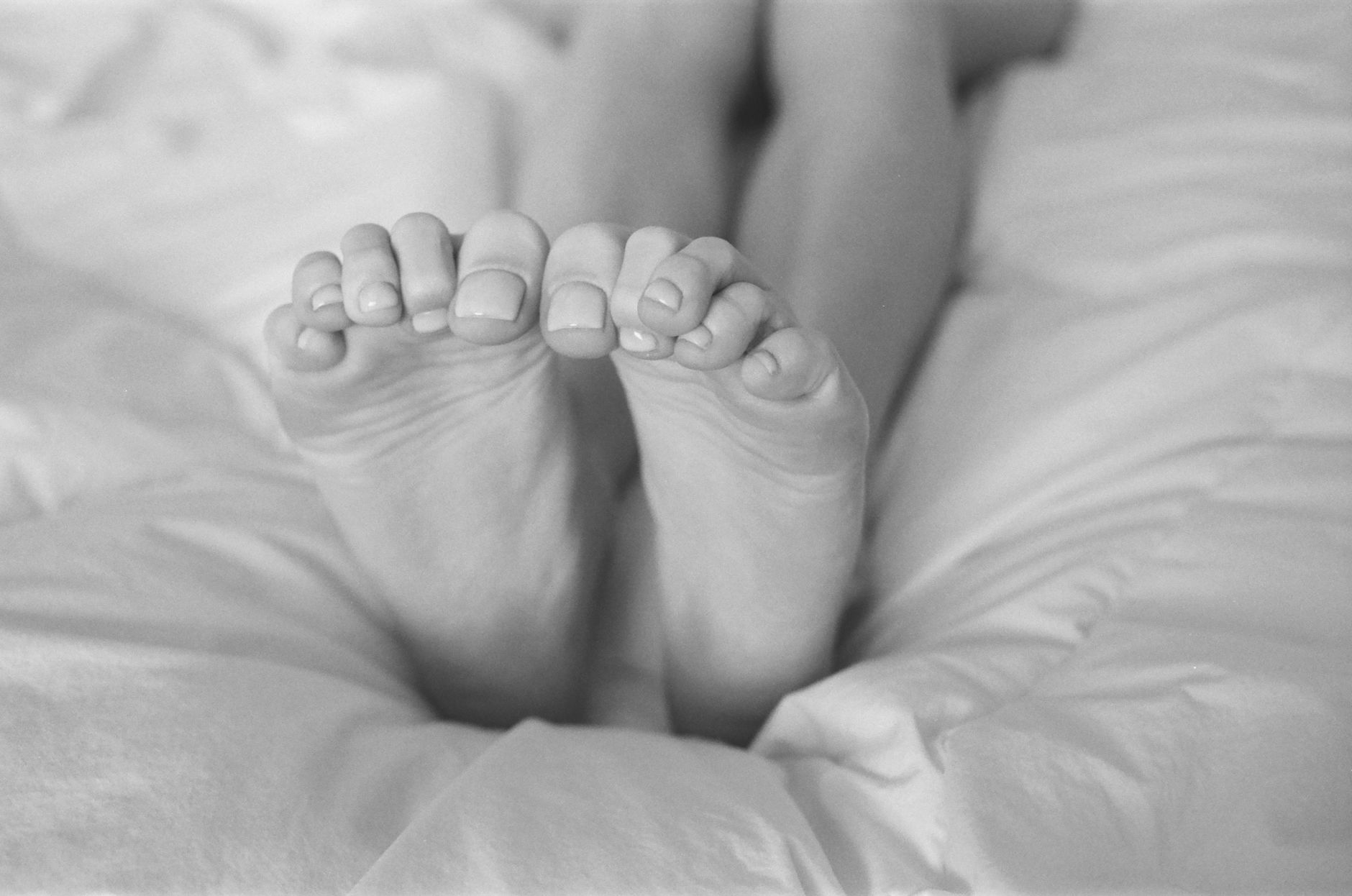 失眠原因大解密:對抗現代壓力的實戰指南 Monochrome close-up of bare feet on a cozy bed, showcasing relaxation.