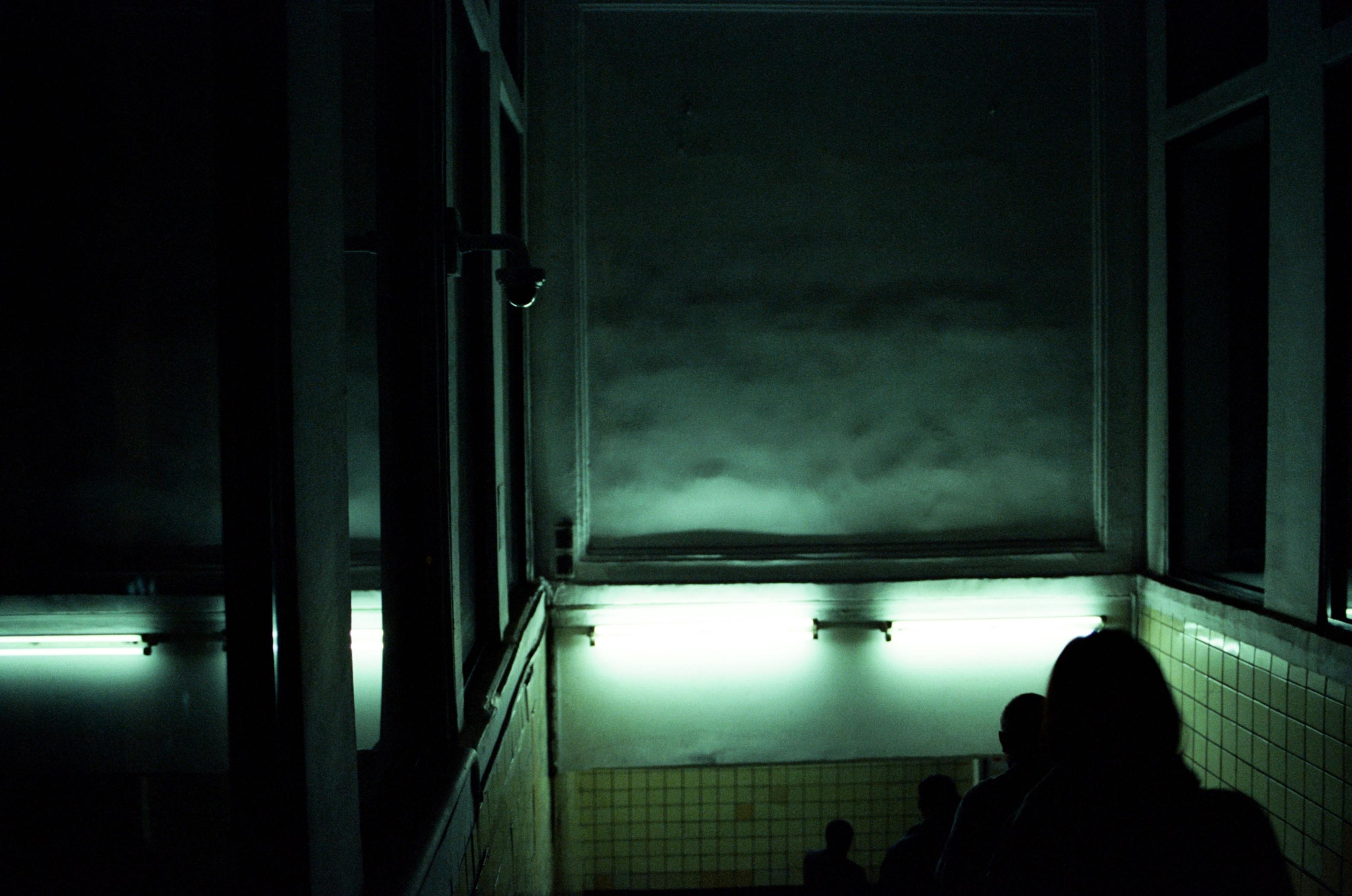 A dimly lit underground passage with silhouettes of people walking down the stairs, creating a moody atmosphere.