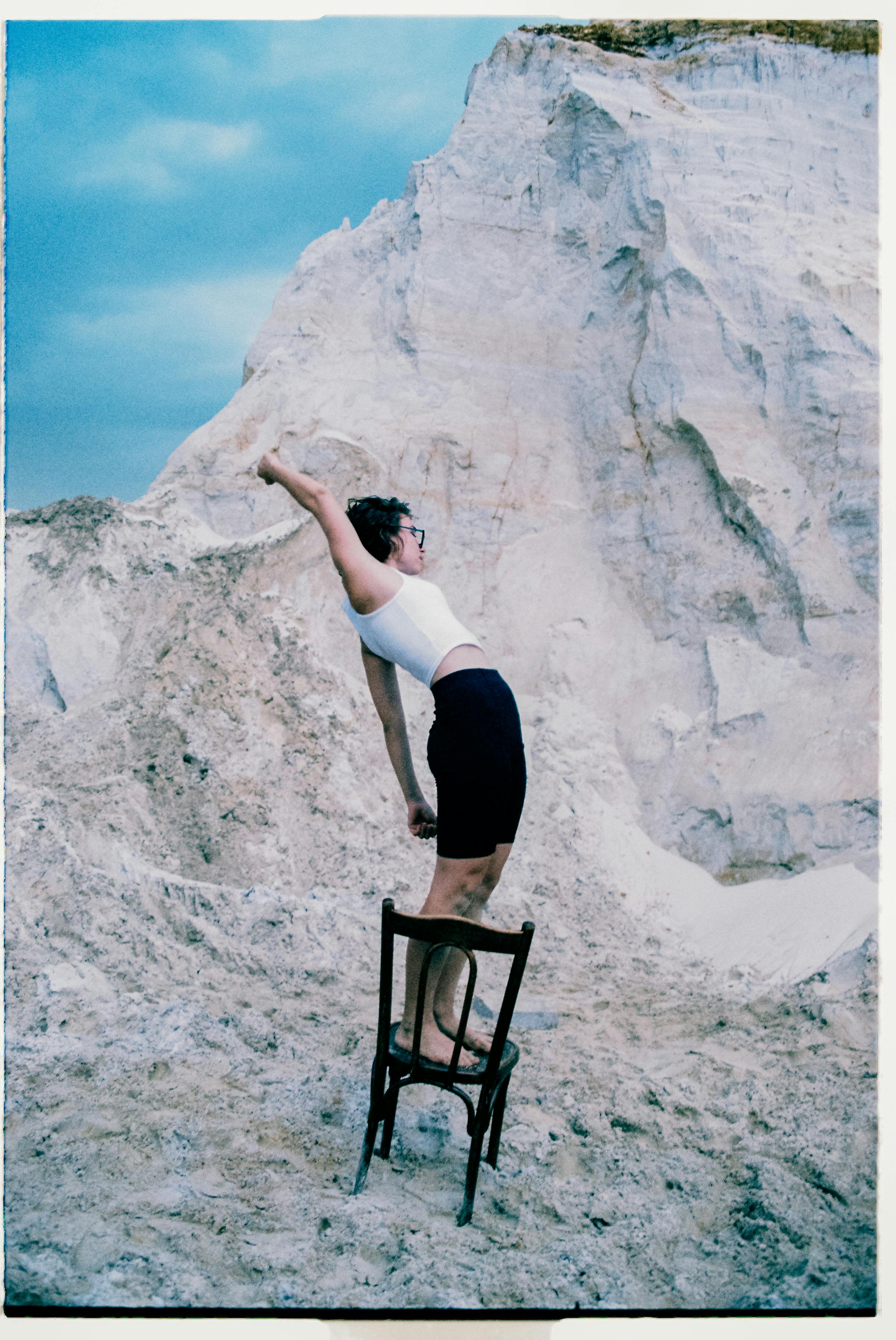 Artistic image of woman on chair in a rocky outdoor setting under a cloudy sky.