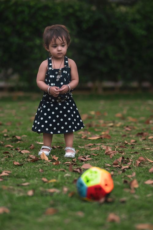 Free Adorable toddler in a polka dot dress plays outside with a colorful ball. Stock Photo