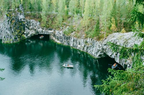 Free Kayakers explore tranquil waters surrounded by rocky cliffs and lush forest in Karelia, Russia. Stock Photo