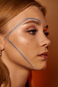 Close-up portrait of a young woman with creative makeup highlighting her cheekbone.
