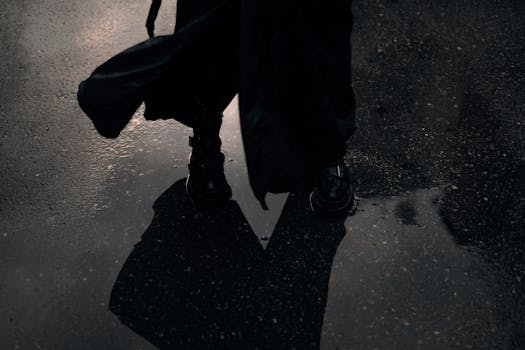 Dark and moody photo of a person standing on wet pavement, casting a reflection.