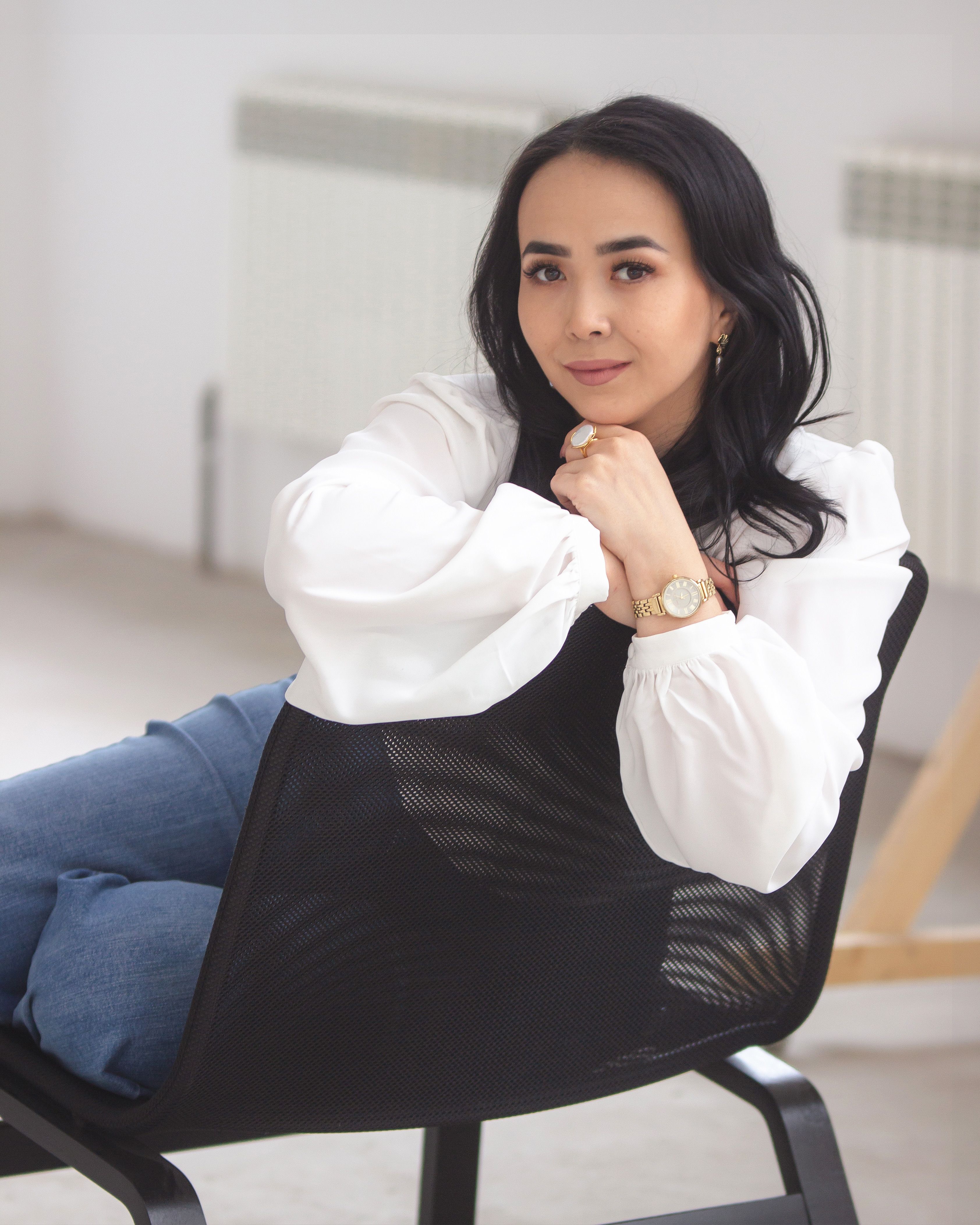 Stylish woman with black hair sitting in modern chair indoors. Portrait with soft lighting and relaxed pose.