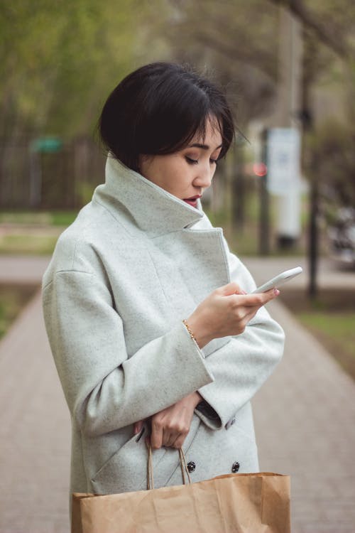 A Woman Wearing a Coat while Holding Her Mobile Phone