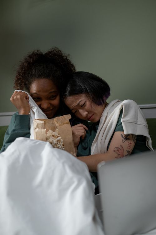 Free Two diverse women watching a scary movie together, sharing a fearful moment. Stock Photo