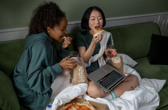 Two people watching a film on a laptop with pizza and popcorn
