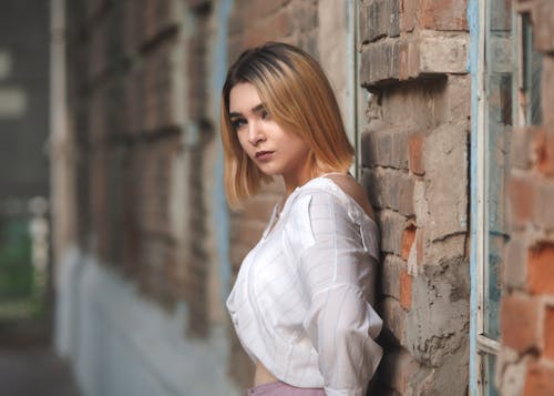 A Woman in White Top Leaning on a Brick Wall