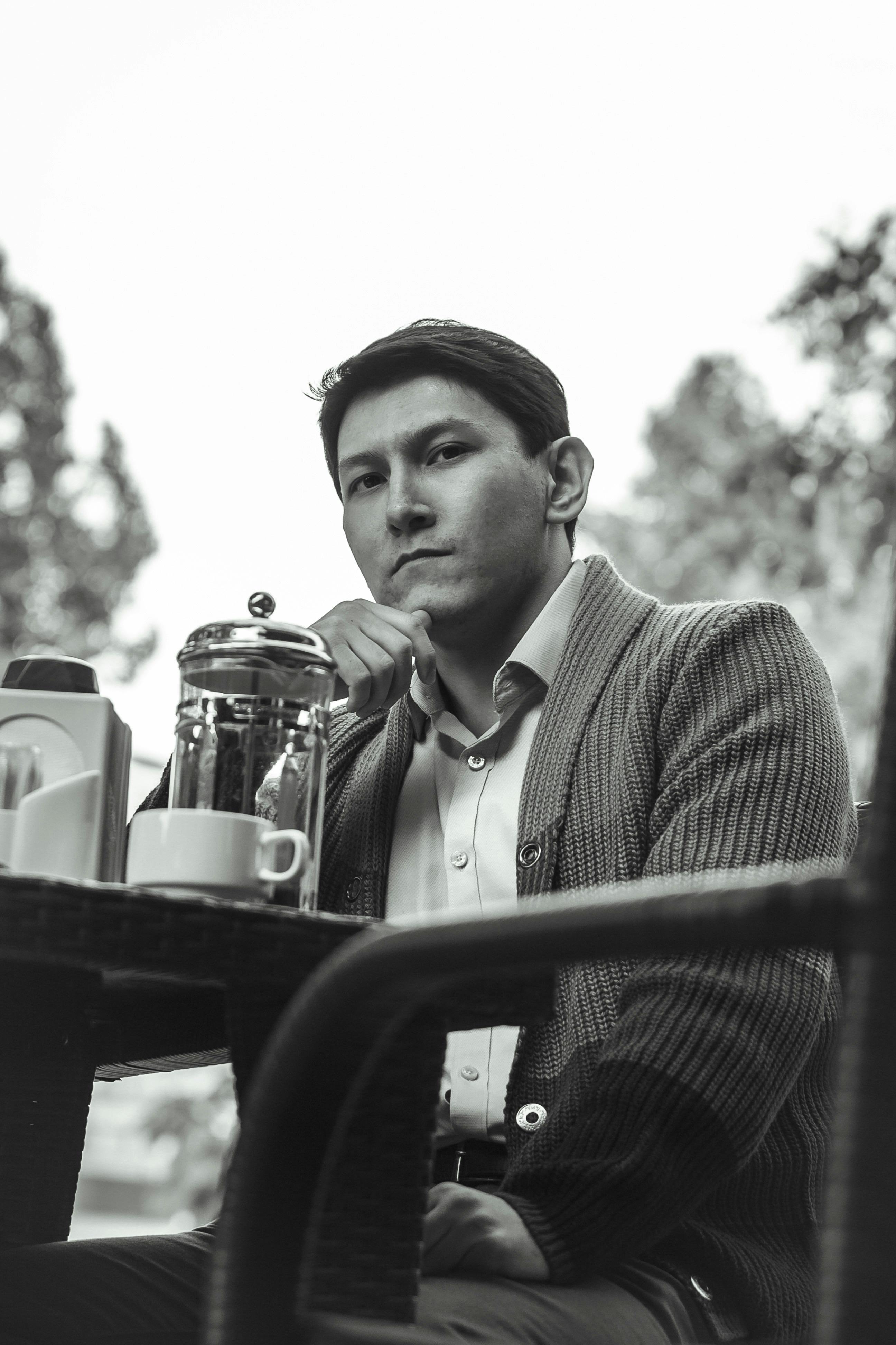 A serious man sitting outdoors in grayscale photography with coffee.
