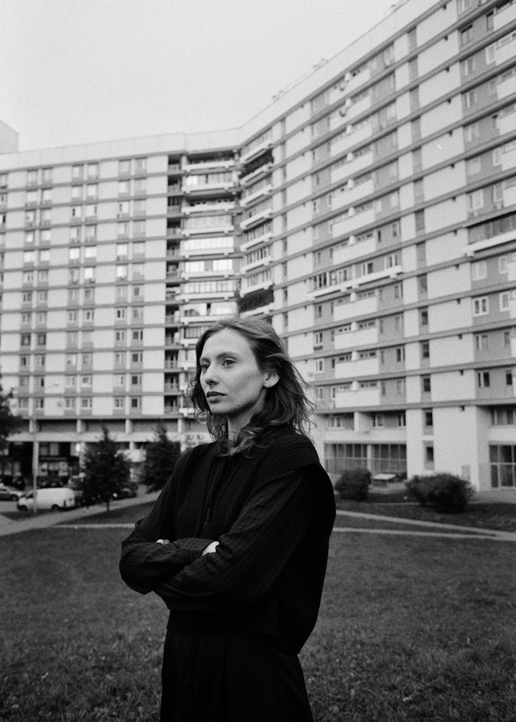 Woman Standing With Folded Hands Before Huge Residential Building