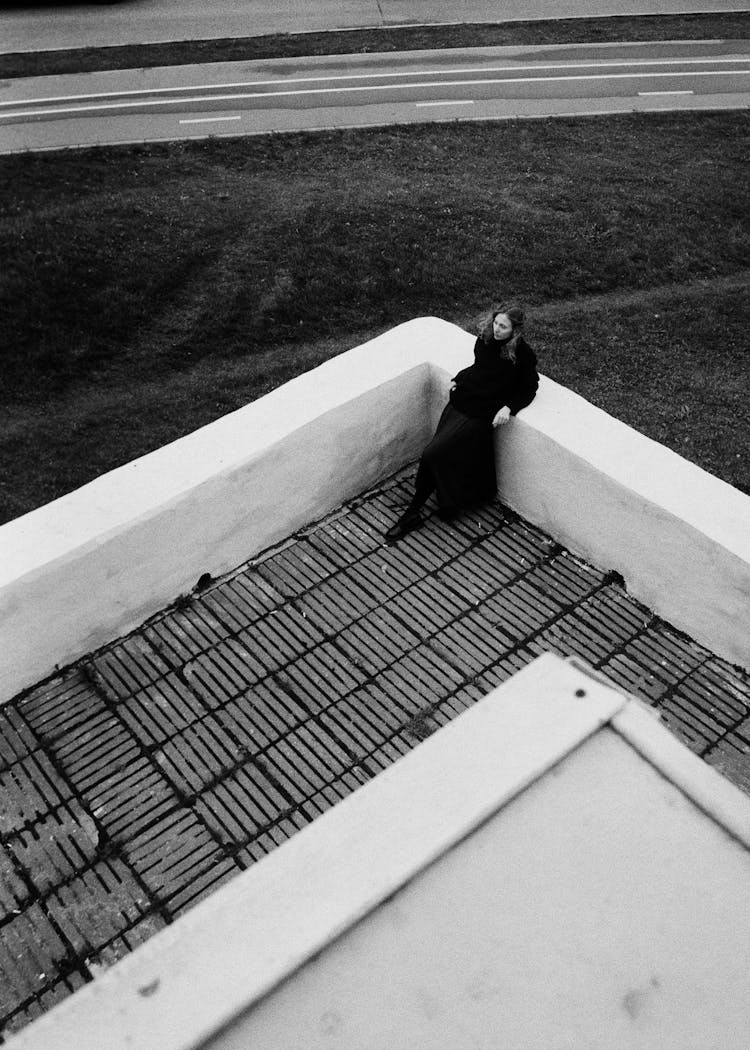 Woman Wearing Long Coat Resting In Corner Of Building Terrace