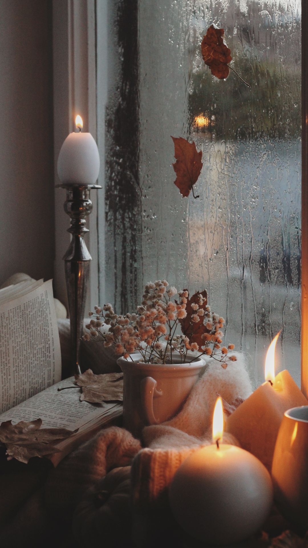 Warm autumn still life with candles, books and raindrops by the window wallpaper