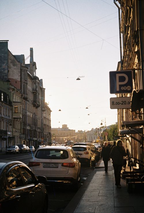Free A lively city street scene with historic architecture, parked cars, and pedestrians during the day. Stock Photo