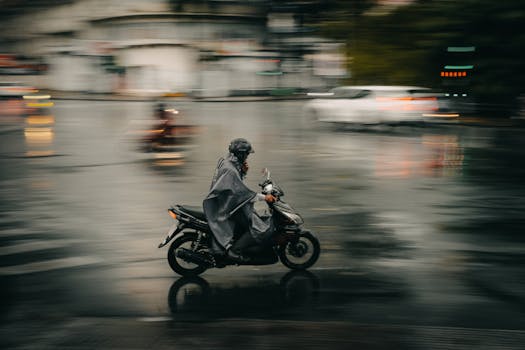 A motorcyclist in a raincoat rides through a wet city street, capturing motion and speed during a rainy day.