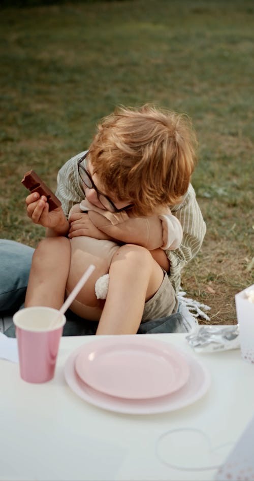 A Young Boy Eating Chocolate while Hugging His Stuff Toy