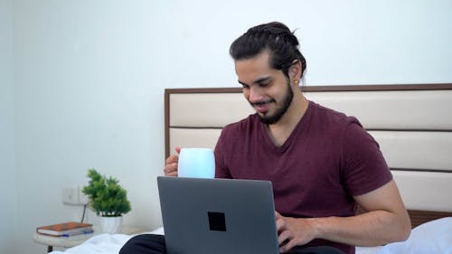 Man Drinking from a Cup While Using a Laptop