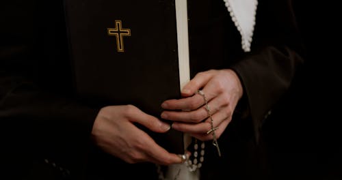 A Woman Holding a Bible and Rosary while Wearing a Cross Earrings