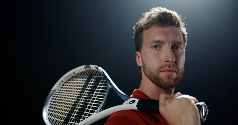 Tennisspieler in einem dunklen Studio mit Schläger über der Schulter