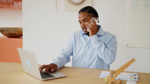 Man Typing on a Laptop While Talking on the Phone