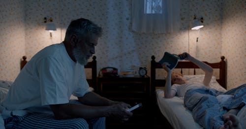 Boy Reading a Book While the Man is Using His Phone 