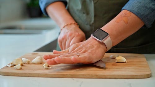 A Person Crushing Garlic on a Wooden Chopping Board