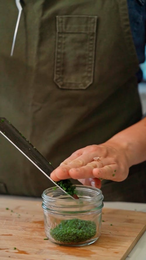 A Person Placing Chopped Chives in a Glass Jar