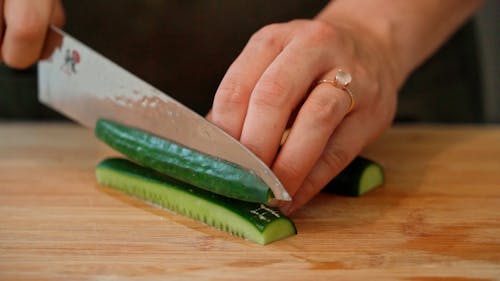 A Person Slicing a Cucumber Using a Kitchen Knife
