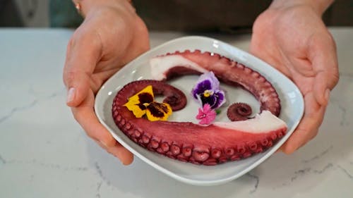 A Person Placing an Octopus Dish on a Marble Surface