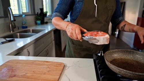 A Person Putting a Raw Fish on a Frying Pan