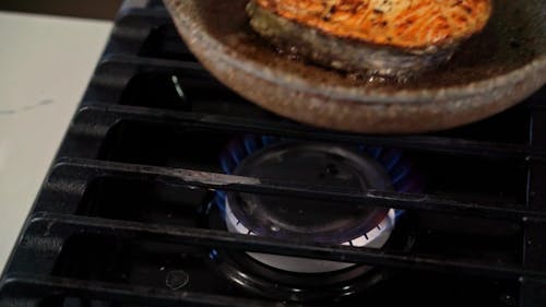 A Person Putting a Frying Pan with Fish on a Gas Stove