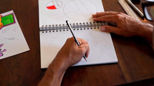 High Angle Shot of a Person Drawing in a Spiral Notebook