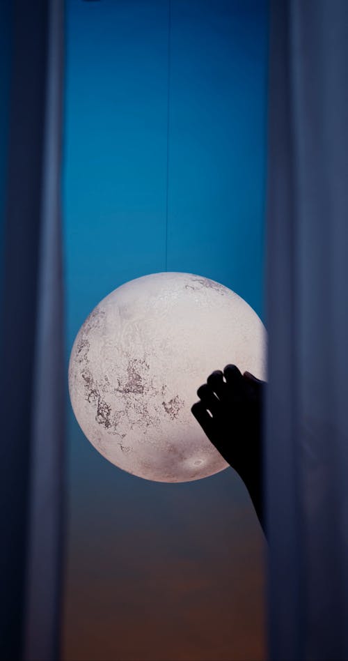 Hand Touching Moon Decoration behind Curtain