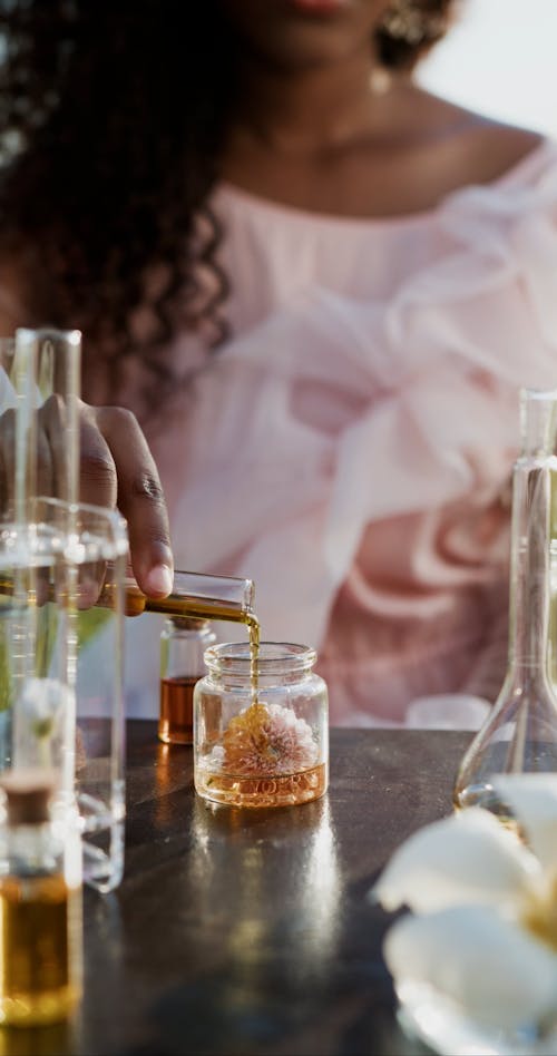 A Person Pouring Oil into a Flower in a Glass Jar