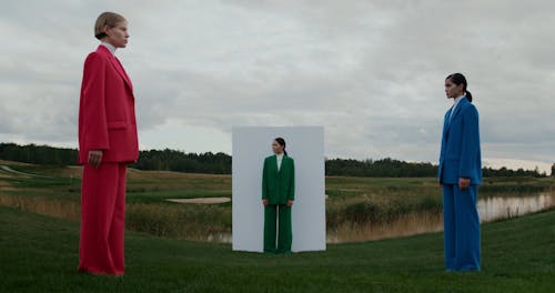 Women in Suits Standing and Walking by Wall on Grass